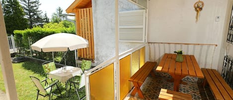 A patio area with a wooden table and benches, a white umbrella, and a small garden with a chair.