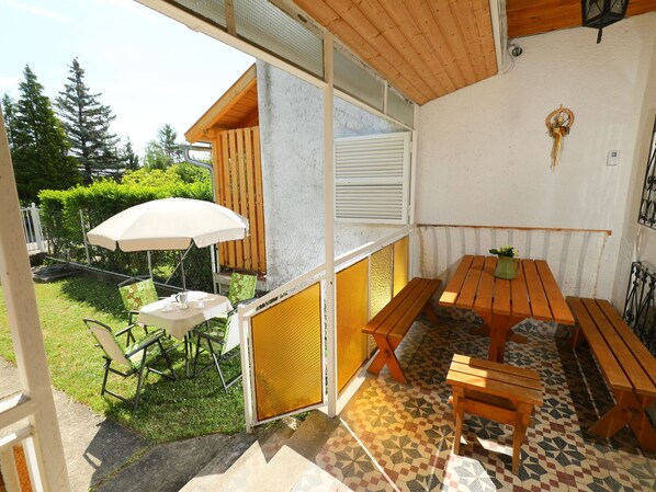 A patio area with a wooden table and benches, a white umbrella, and a small garden with a chair.