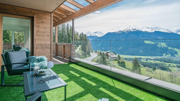 Una habitación moderna con una mesa y sillas de vidrio, techo de madera y vistas a la montaña.