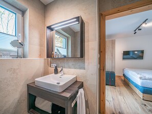 A modern bathroom with a large mirror, a sink, and a wooden vanity. - Luxury apartment with sauna near the ski lift (Mittersill)