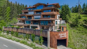 Un hotel de varios pisos con fachada de madera y balcones, rodeado de vegetación y un cielo despejado.