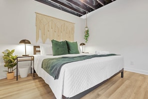 Une chambre à coucher moderne avec un lit, des tables de chevet, une plante suspendue et une décoration murale en macramé.