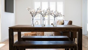 A dining table with three vases of flowers and a bench in a bright room with a window and a sofa in the background. - Getaway on Curran. EV + Firepit. Walk to CBD. (Orange)