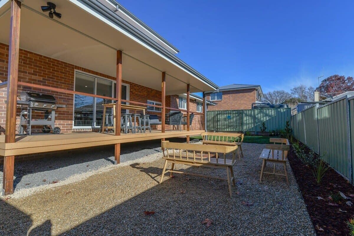 Ein überdachter Patio-Bereich mit Grill, Sitzgelegenheit und Blick auf ein Backsteinhaus.