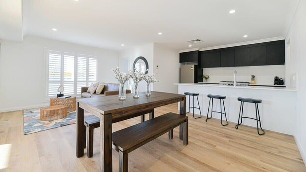 A modern kitchen with dark cabinets, a wooden dining table, and bar stools. - Getaway on Curran. EV + Firepit. Walk to CBD. (Orange)