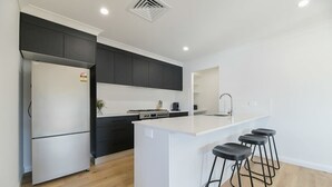 A modern kitchen with a central island, black cabinets, a stainless steel refrigerator, and a sink. - Getaway on Curran. EV + Firepit. Walk to CBD. (Orange)
