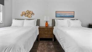 A hotel room with two beds, a nightstand with a lamp, a decorative wall piece, and a painting of a beach scene.