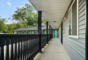 Guests may walk along the covered path to the building, which features a green door and windows.