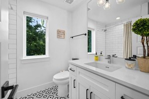 Ein modernes Badezimmer mit weißem Waschtisch, Toilette, einem großen Spiegel und einem Fenster mit Blick ins Grüne.