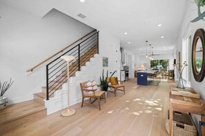 A spacious living area with a staircase, wooden flooring, and modern furniture.