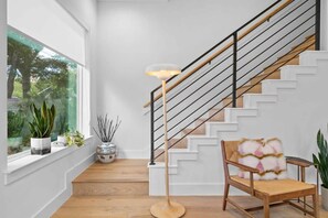 Een trap met een houten leuning en zwarte balustrades, die leidt naar een plateau met een stoel en een vloerlamp.