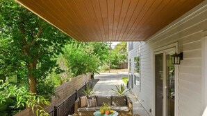 A covered outdoor seating area with wicker furniture, a round table, and a potted plant. - Cherrywood Home Near UT / ATX / Private Backyard (Austin)