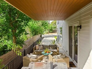 Eine überdachte Terrasse mit Korbmöbeln, einem kleinen Tisch mit einer Pflanze und einer Schiebetür.