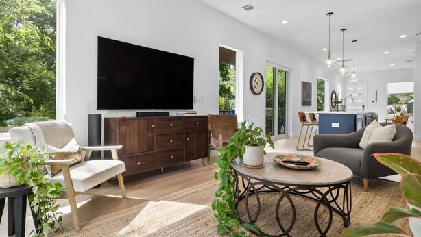 A modern living room with a flat-screen TV, wooden furniture, and a large window. - Cherrywood Home Near UT / ATX / Private Backyard (Austin)