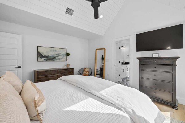 A bedroom with a bed, a dresser, a mirror, and a flat-screen TV.