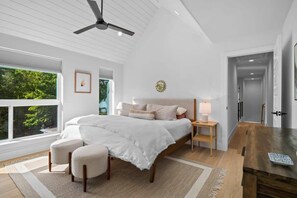Ein Schlafzimmer mit einem Bett, Nachttischen, einem Fenster mit Jalousien, einem Deckenventilator und Blick auf Grün.