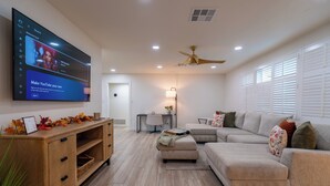 A modern living room with a flat-screen TV, a wooden entertainment unit, a beige sectional sofa, and a ceiling fan. - Luxurious Cascada Oasis ~ Cozy ~ Games ~ King Beds (Litchfield Park)