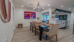 A modern dining area with a large TV, wooden flooring, and a chandelier. - Luxurious Cascada Oasis ~ Cozy ~ Games ~ King Beds (Litchfield Park)