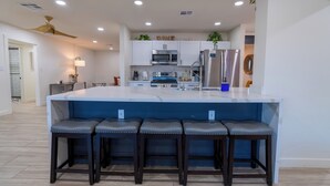 A modern kitchen with white cabinets, a central island with bar stools, and a ceiling fan. - Luxurious Cascada Oasis ~ Cozy ~ Games ~ King Beds (Litchfield Park)