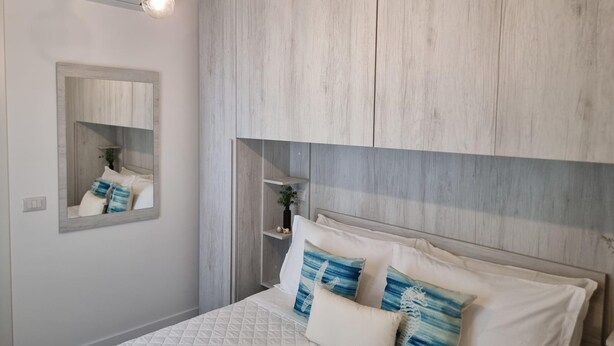 A bedroom with a bed, a mirror, and wooden paneling on the wall. - Piccolo Nida 18 in Cattolica (Cattolica)
