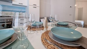 A modern dining area with a white table set for four, featuring blue plates and clear glassware. - Piccolo Nida 18 in Cattolica (Cattolica)