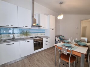 A modern kitchen with white cabinets, a gas stove, and a dining area with a table set for four. - Piccolo Nida 18 in Cattolica (Cattolica)