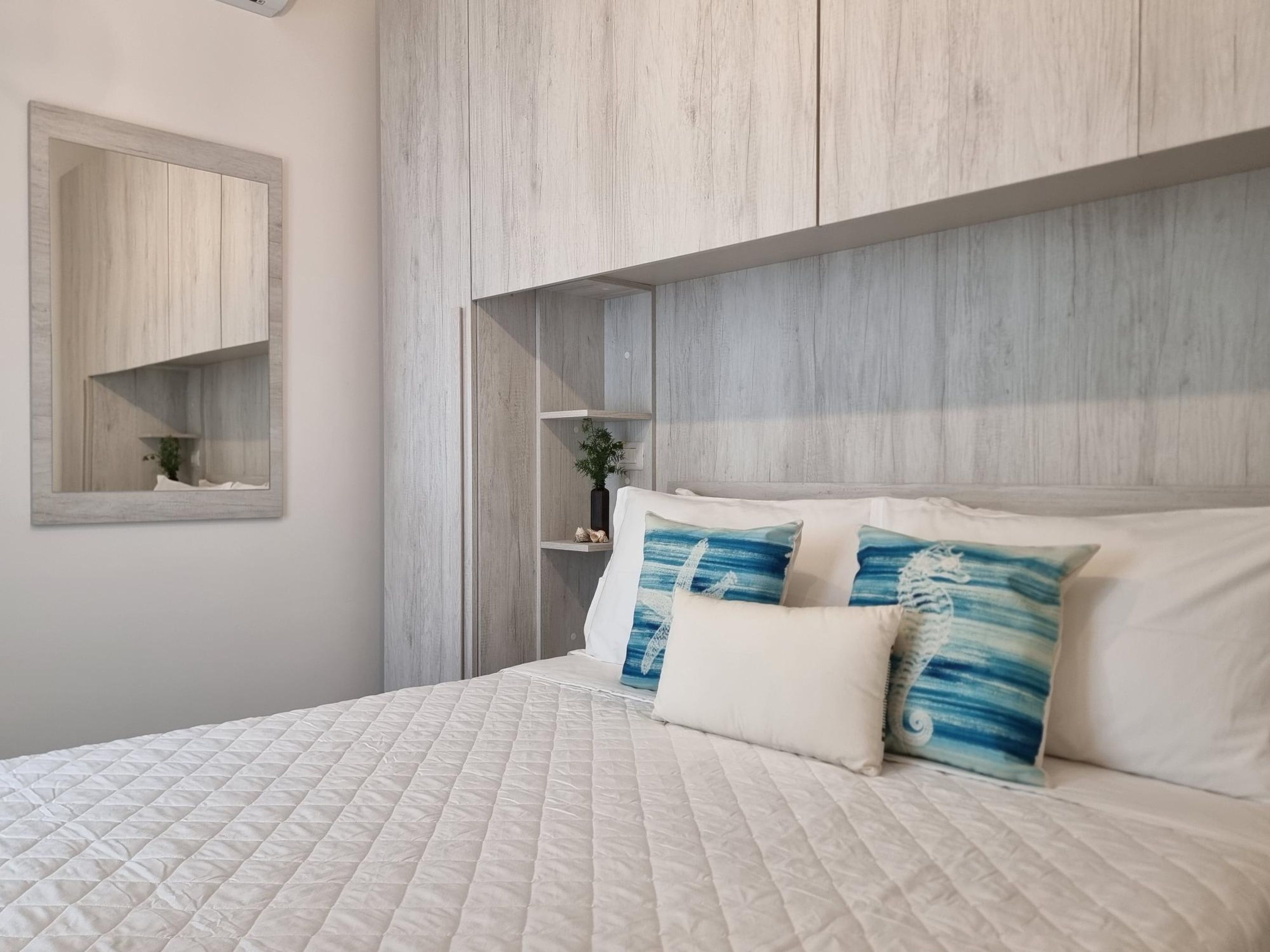 Una camera da letto con un letto grande, una testiera in legno, un piccolo ripiano con una pianta e uno specchio a parete.