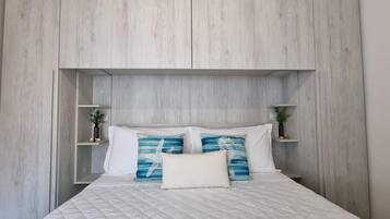 Una camera da letto con un letto, biancheria bianca e una testiera con scaffali integrati.