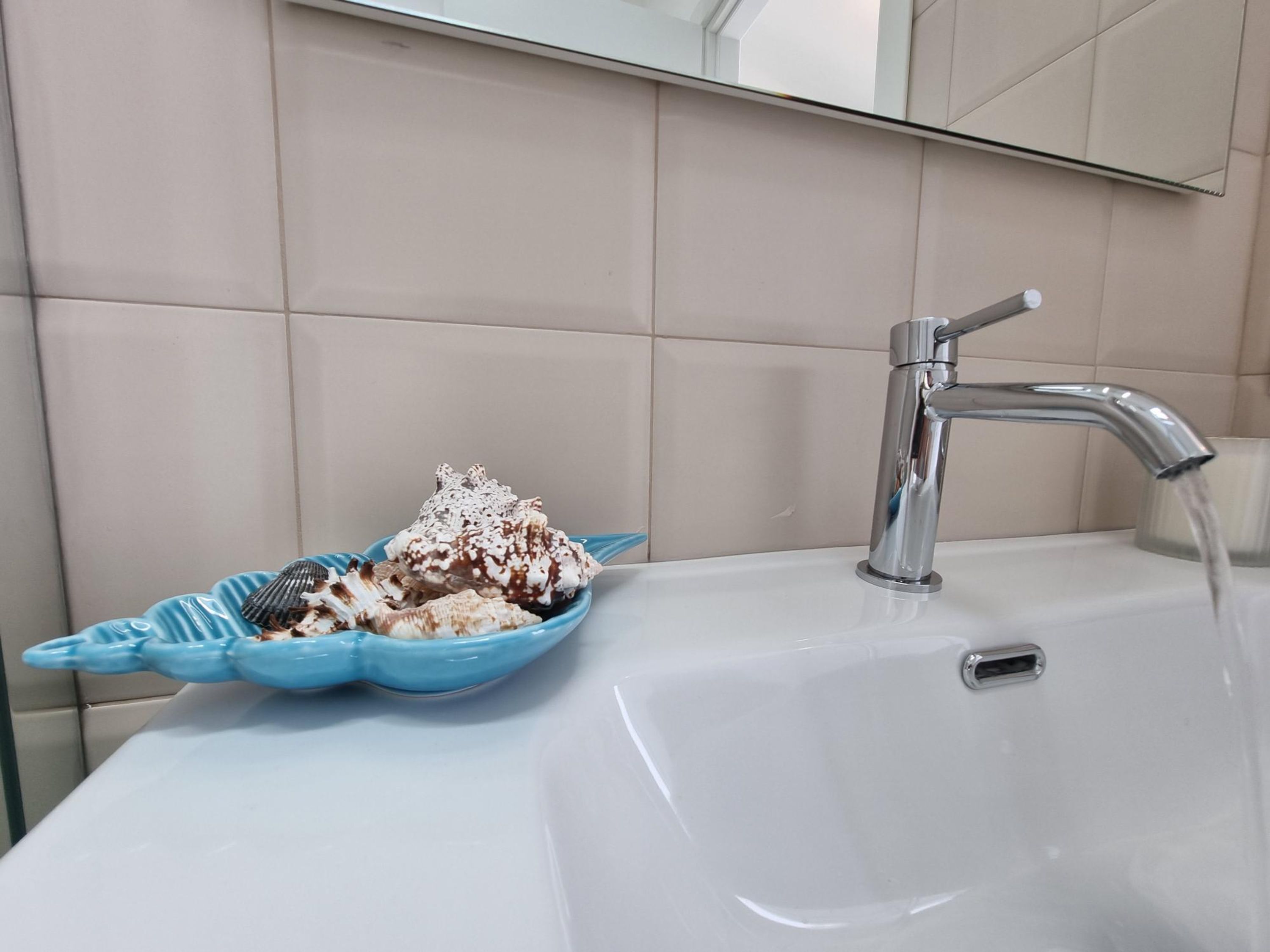 A bathroom sink with a blue decorative bowl containing seashells and a chrome faucet.
