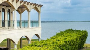 A covered outdoor area with a view of a lake, supported by columns and featuring a glass railing. - Villa Castello- Water Views Resort Amenities (Placencia)