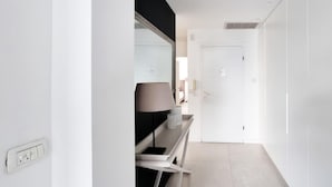 A narrow hallway with a white door at the end, a lamp on a table, and a power outlet on the wall. - Hovevei Tsiyon Magnolia (Tel Aviv)