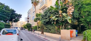 A street with buildings, a white car, and a person walking. - Hovevei Tsiyon Magnolia (Tel Aviv)