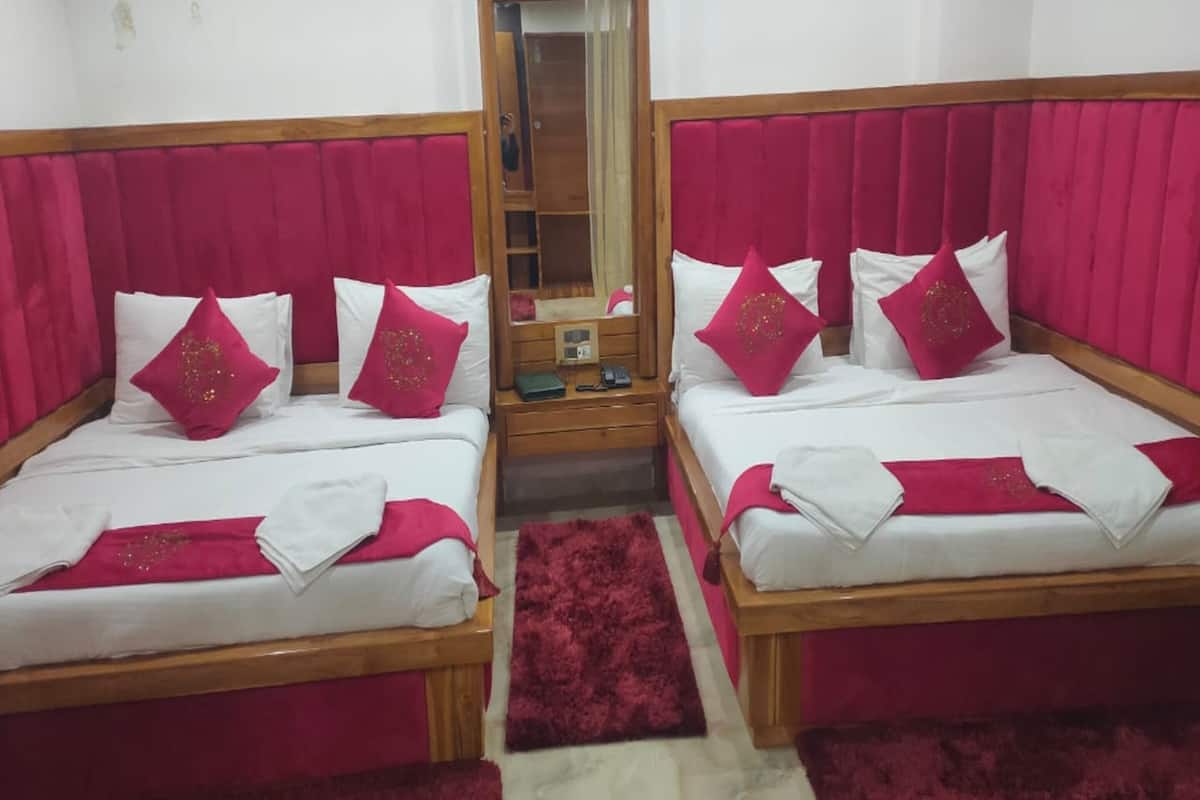 Une chambre avec deux lits, chacun doté d’un cadre en bois et d’une tête de lit rouge. Un miroir est placé entre les lits, et un appareil de climatisation est fixé au mur.