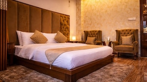 A spacious bedroom with a large bed, two armchairs, a wooden headboard, and a patterned wall. - Hotel Saheb's Castle - Best Mountain View & Jacuzzi Suites, McLeodganj (Dharamshala)