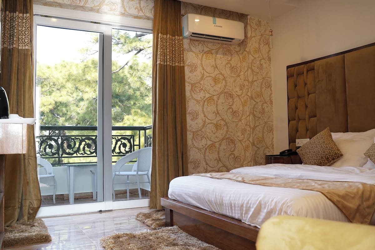 Une chambre avec un grand lit, une table de chevet, une chaise et un balcon donnant sur la forêt.