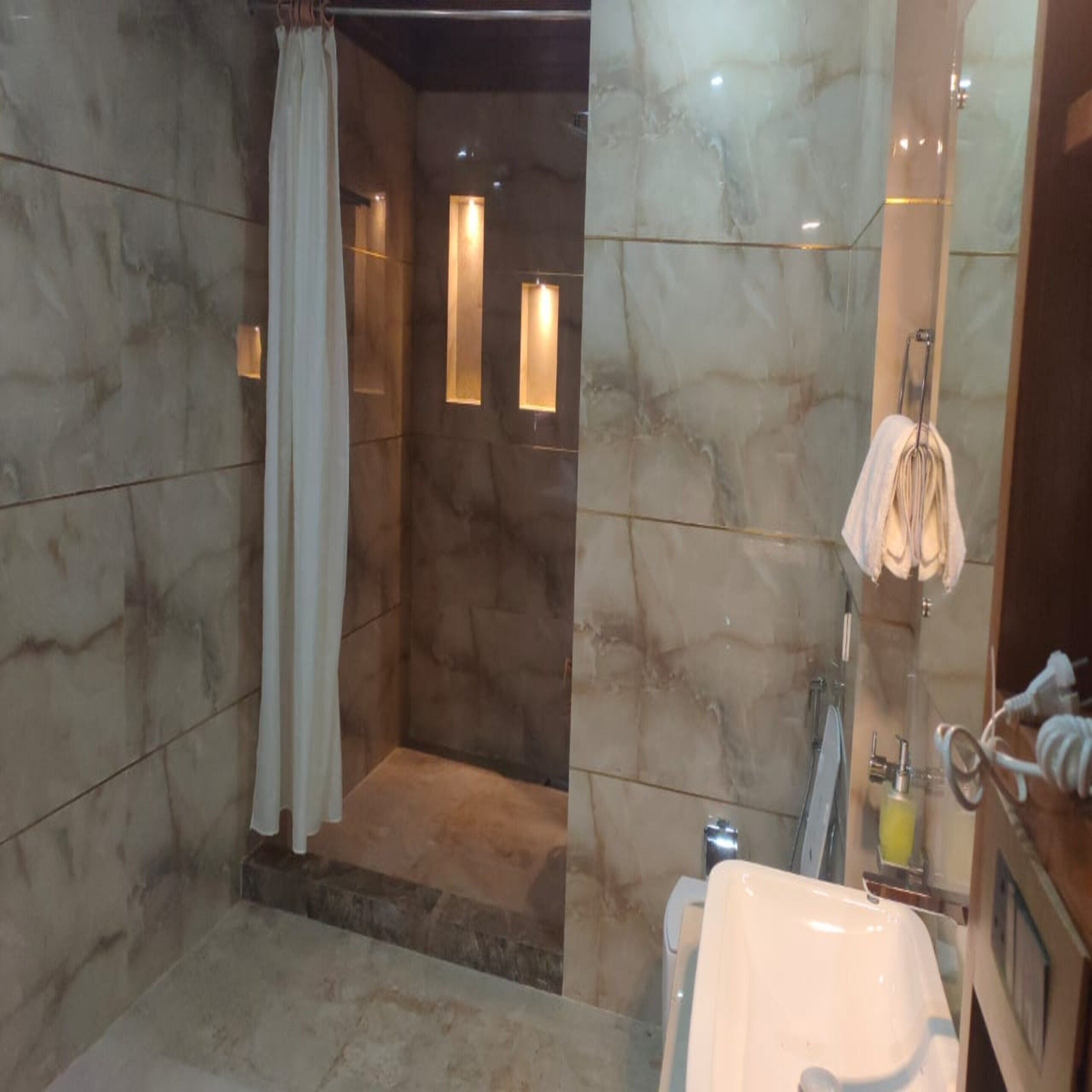 A modern bathroom with a marble floor, a shower area with a curtain, a sink with a mirror, and a towel rack.