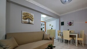 En stue med en beige sofa, et glasbord og et spiseområde med bord og stole.