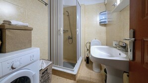 Et badeværelse med bruser, toilet, håndvask og vaskemaskine.