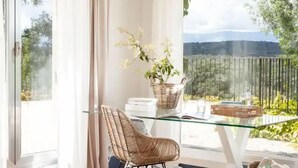 A modern room with a glass table, wicker chair, and a view of a mountainous landscape. - Luxury villa on a private estate in Toledo w/pool and views of Sierra de Gredos. (mejorada)