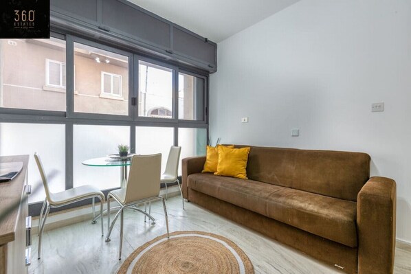 A modern living room with a brown sofa, two chairs, a glass table, and a large window.
