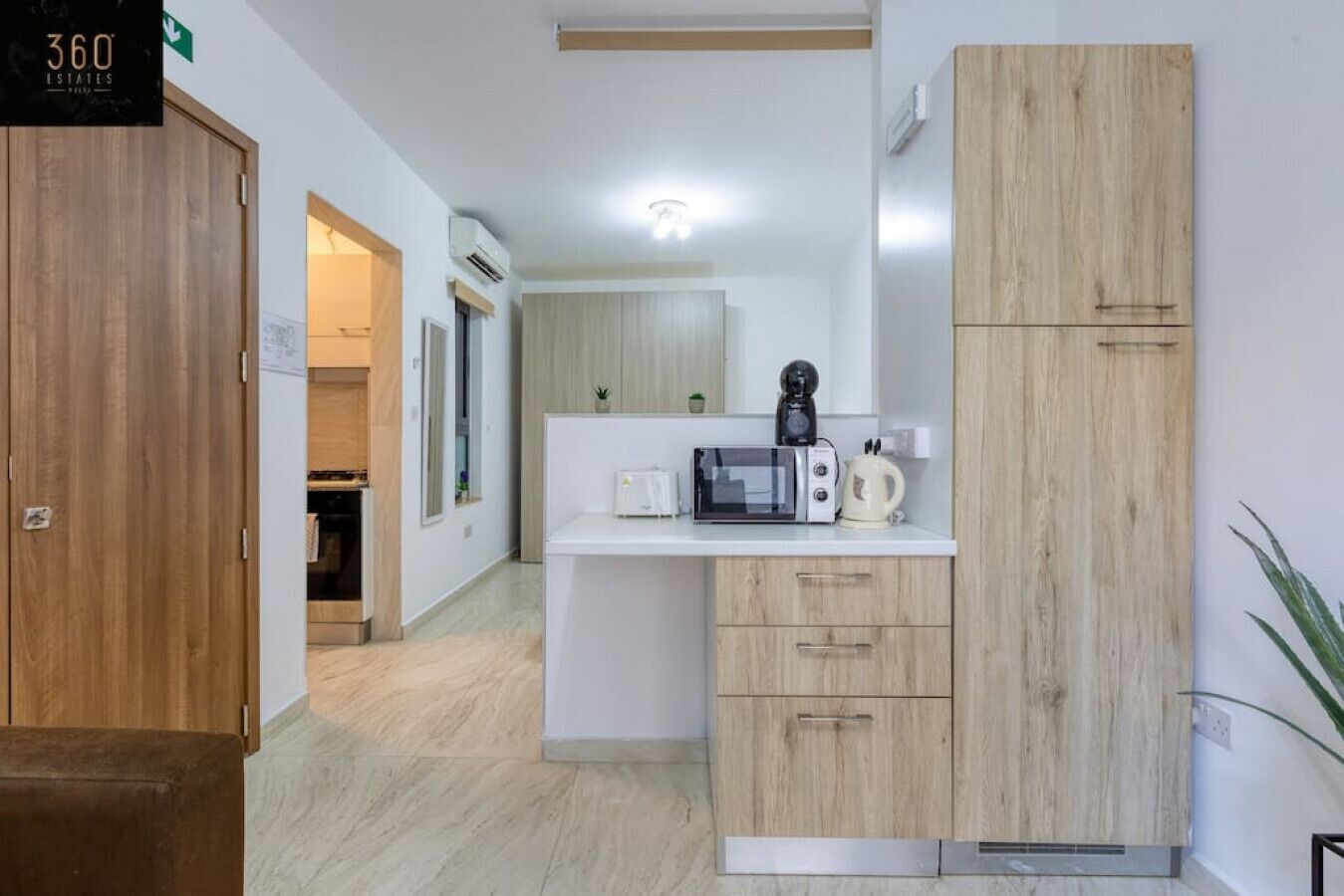A modern kitchen with a microwave, kettle, and wooden cabinets.