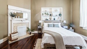 A bedroom with a fireplace, a bed, bedside tables, and a shelving unit. - Comfort Suite | Near Mercer University & Downtown (Macon)