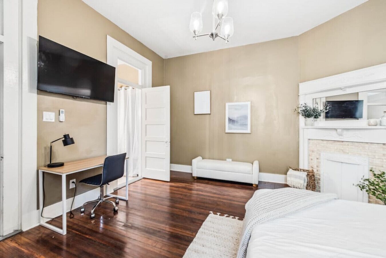 A bedroom with a bed, a desk, a chair, a television, a fireplace, and a door.