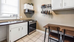 A compact kitchen with white cabinets, a stove, a microwave, and a pot rack. - Comfort Suite | Near Mercer University & Downtown (Macon)