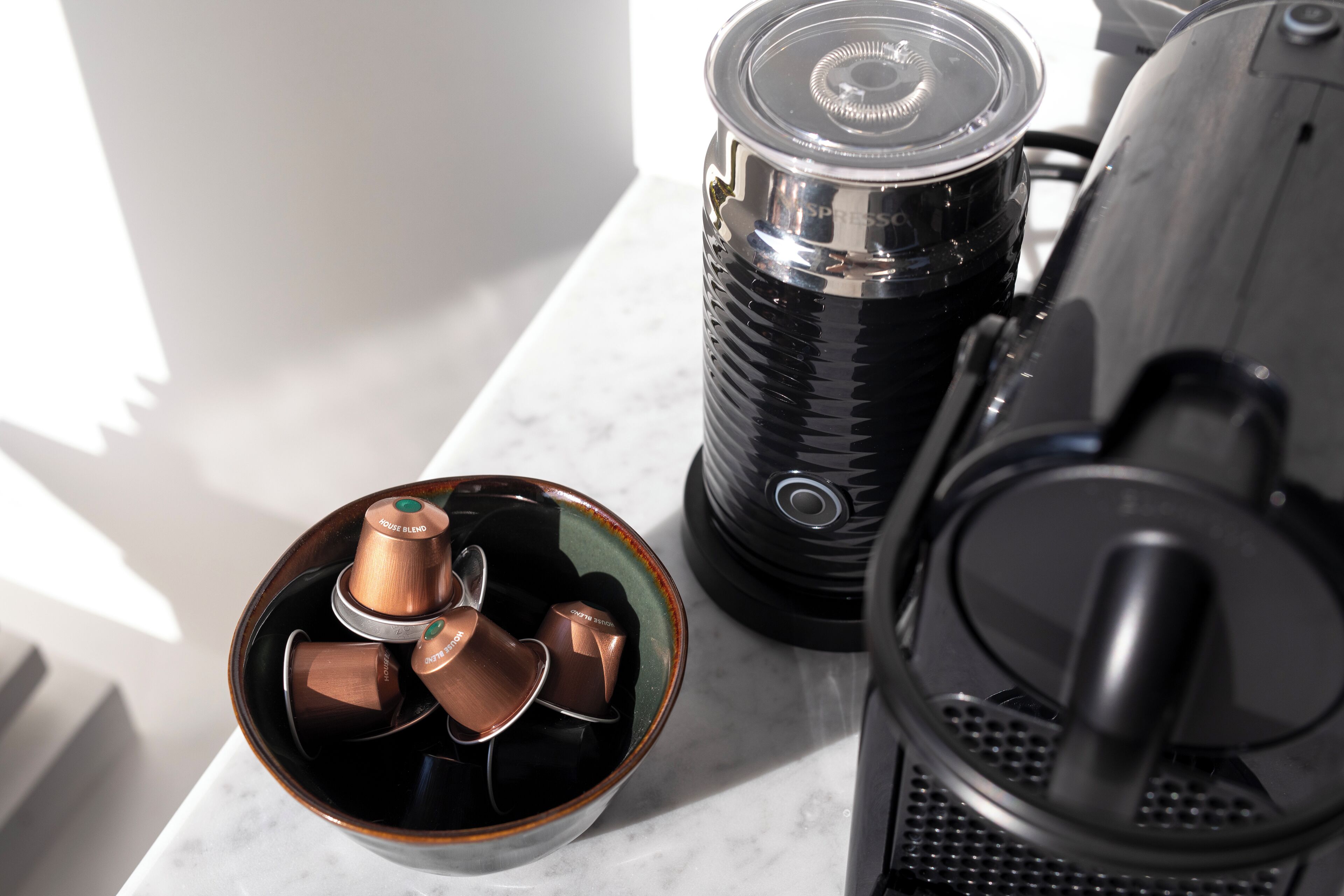 Eine Kaffeemaschine, eine Kaffeetasse und eine Kapselbehälter auf einer Marmorarbeitsplatte.