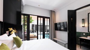 A modern hotel room with a large bed, a TV mounted on the wall, a bathroom with a sink and mirror, and a view of the outdoor area. - Martini Beachside 1 (Canggu)