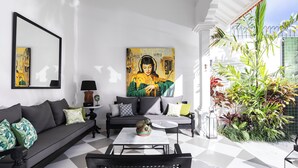 A modern living room with a sofa, coffee table, and chairs. There is a large painting on the wall and a potted plant on the balcony. - Martini Beachside 1 (Canggu)