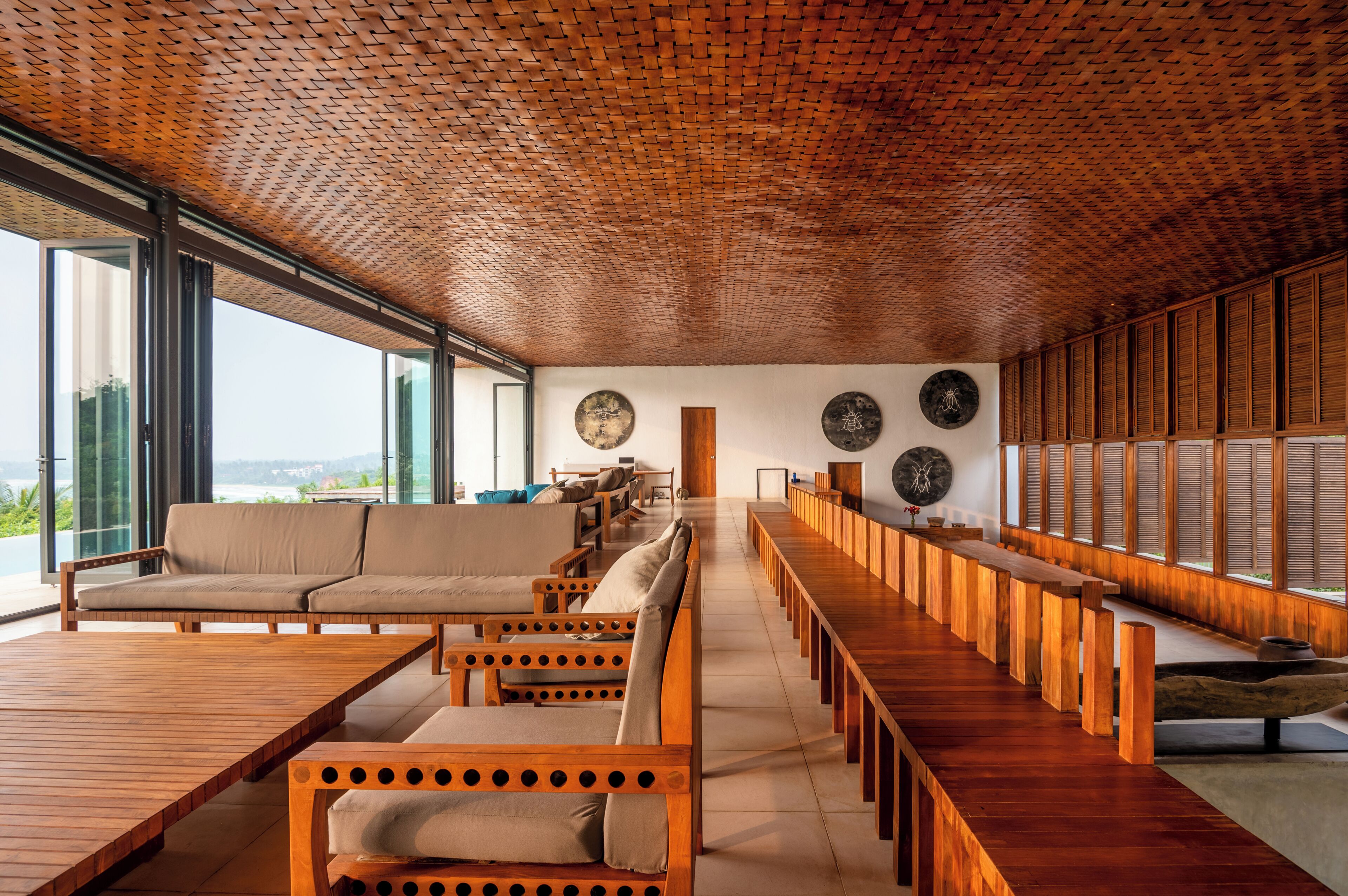 A modern interior with a long wooden bench, a sofa, and a dining area.