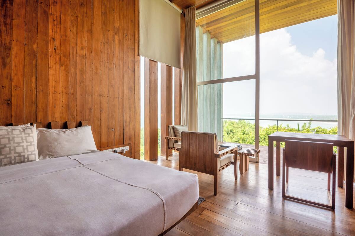 Een slaapkamer met een groot bed, houten wanden, uitzicht op het omliggende landschap en een houten bureau.