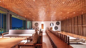 A modern interior with a long wooden bench seating area, a sofa, and a view of the cityscape through large windows. - Villa Vista by The Serendipity Collection (Mirissa)